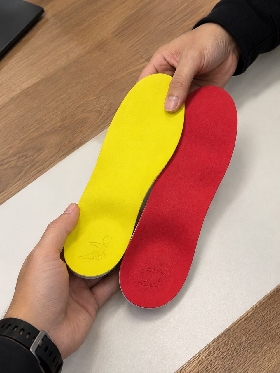 Manos sosteniendo dos plantillas personalizadas de Biosports, una amarilla y una roja